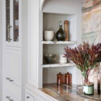 The elevated new traditional kitchen features 48-inch range with Tudor style arched hood. Full height quartzite backsplash with rose and caramel veining. Range area has recessed spice niches.