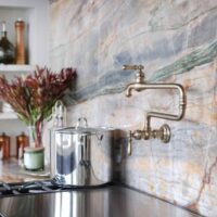 The elevated new traditional kitchen features 48-inch range with Tudor style arched hood. Full height quartzite backsplash with rose and caramel veining. Range area has recessed spice niches; brushed bronze pot filler.