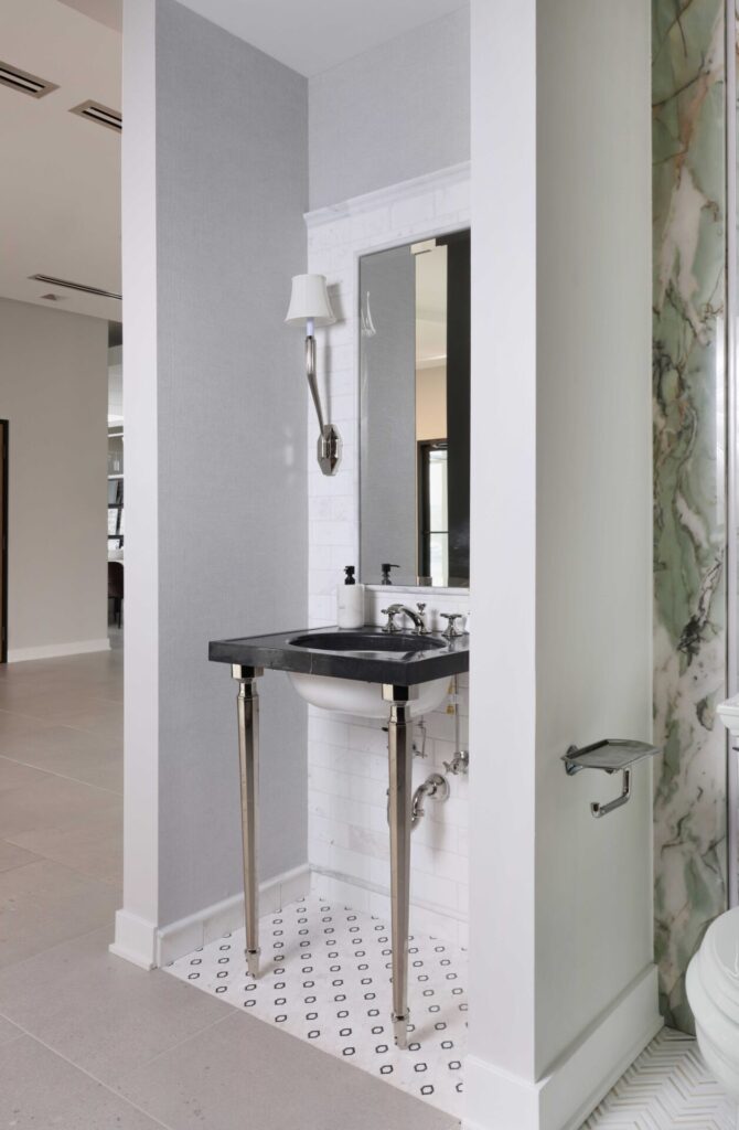 The luxury powder room features a console sink with a striking black marble top, a black-and-white marble mosaic floor, a sink wall with integrated mirror clad in white marble tile, and polished nickel hardware.