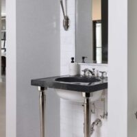 The luxury powder room features a console sink with a striking black marble top, a black-and-white marble mosaic floor, a sink wall with integrated mirror clad in white marble tile, and polished nickel hardware.