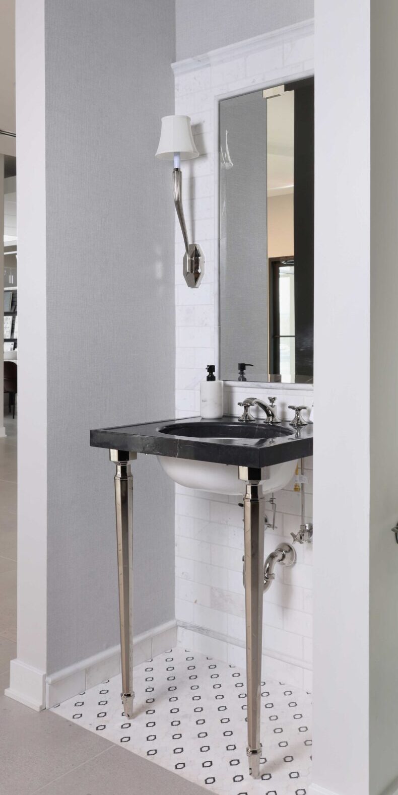 The luxury powder room features a console sink with a striking black marble top, a black-and-white marble mosaic floor, a sink wall with integrated mirror clad in white marble tile, and polished nickel hardware.