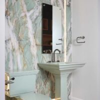 The color revival powder room features a richly veined porcelain slab with integrated lighting and floating mirror, aspen green pedestal sink with titanium and black nickel hardware, and marble herringbone floor.