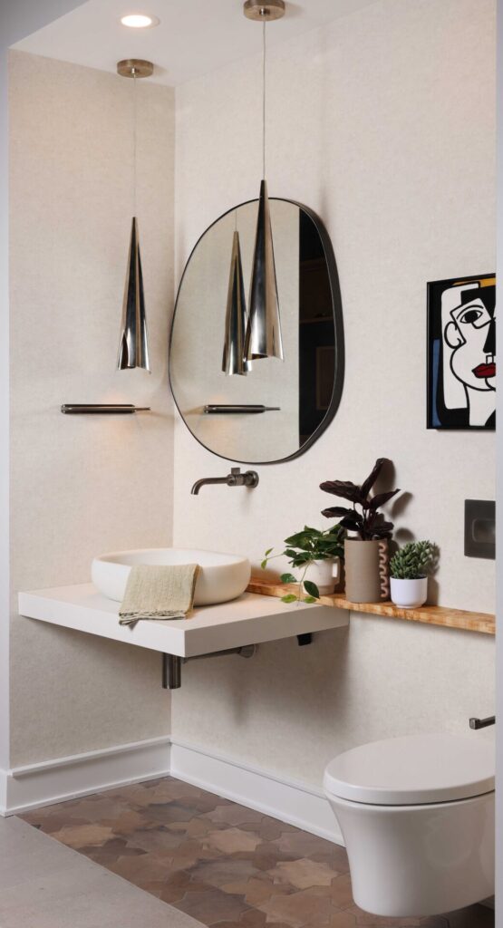 The Modern Mediterranean Powder Room features floating vanity and vessel sink designed to resemble rustic poured concrete; wall mounted faucet in luxe steel finish adding crisp architectural counterpoint. Plaster look wallpaper, burnished steel pendant lights, wall mounted toilet, blackened brass mirror, custom wood ledge, porcelain floor tile designed to mimic terracotta.