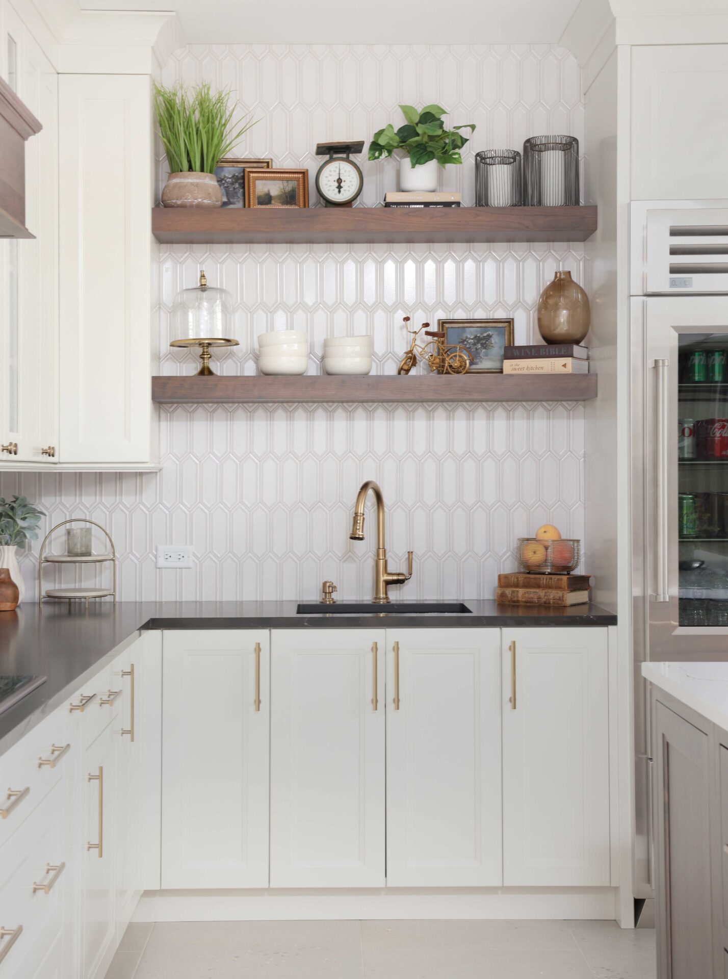 Vintage inspired family kitchen features cherry wood floating shelves, white picket backsplash tile, soft ivory painted cabinets with shaker style doors, black and white quartz countertops, black composite sink, faucet in luxe gold, mixed metal hardware throughout.