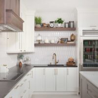 Vintage inspired family kitchen features cherry wood in the island, floating shelves and range hood; white picket backsplash tile, soft ivory painted cabinets with shaker style doors, black and white quartz countertops, pro grade induction cooktop, double ovens, below counter microwave, refrigerator with see-through door, black composite sink, faucet in luxe gold, mixed metal hardware throughout.