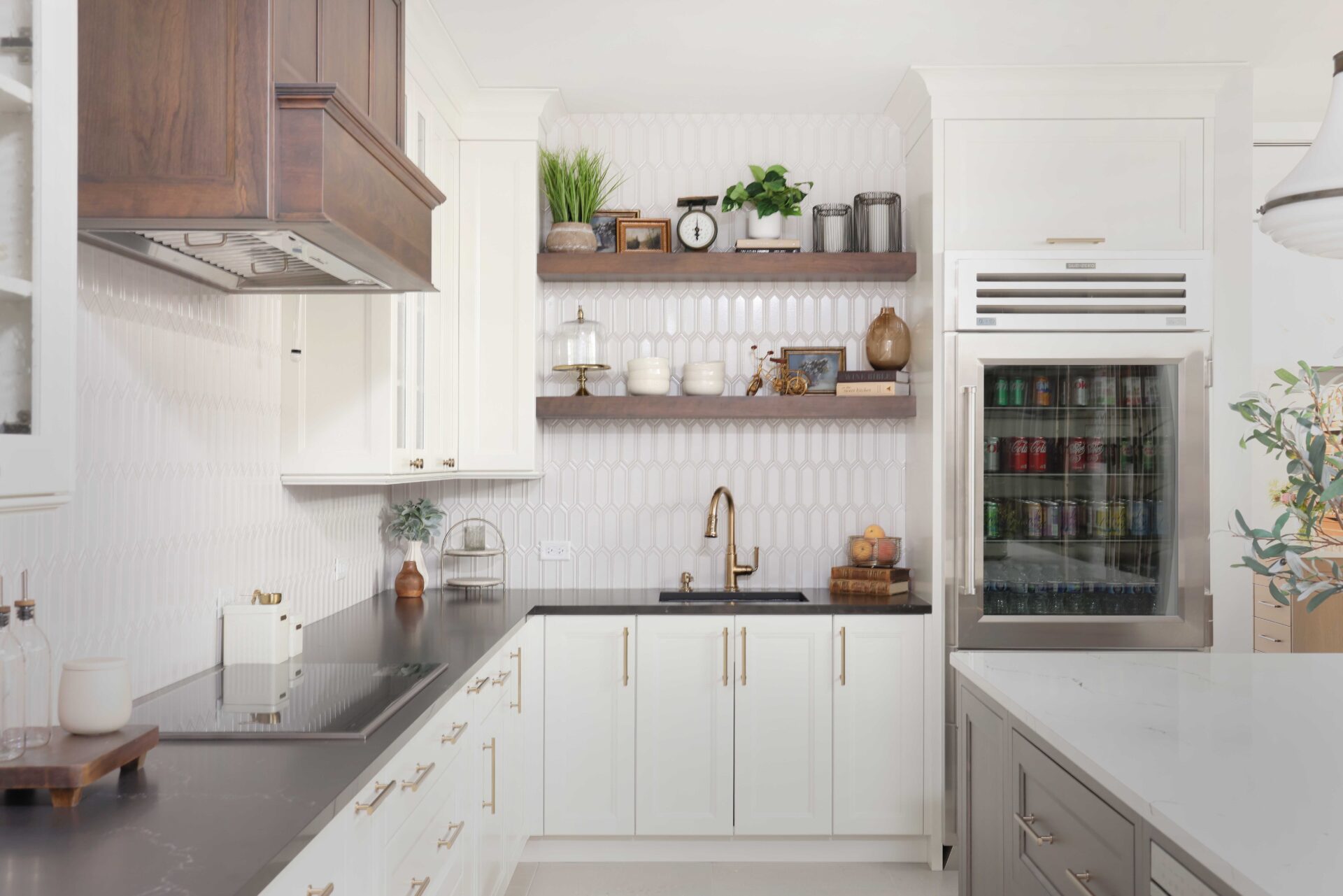 Vintage inspired family kitchen features cherry wood in the island, floating shelves and range hood; white picket backsplash tile, soft ivory painted cabinets with shaker style doors, black and white quartz countertops, pro grade induction cooktop, double ovens, below counter microwave, refrigerator with see-through door, black composite sink, faucet in luxe gold, mixed metal hardware throughout.