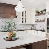 Vintage inspired family kitchen features cherry wood in the island, floating shelves and range hood; white picket backsplash tile, soft ivory painted cabinets with shaker style doors, black and white quartz countertops, pro grade induction cooktop, double ovens, below counter microwave, refrigerator with see-through door, black composite sink, faucet in luxe gold, mixed metal hardware throughout.