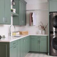 The colorfully classic laundry room features rich green cabinets, floating shelves, subway tile, quartz countertop, gray sink, polished chrome hardware, printed floor tile. Organizational solutions include pull out drying rack, hanging pole for steaming or storing garments, and lots of counterspace for folding.
