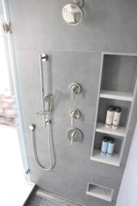 Gray large panel tile shower with polished nickel shower head, triple shower niche and foot shaving niche
