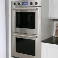 Stacked ovens, stainless steel with black knobs, white cabinet surround