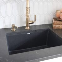 Black sink and countertops with gold faucet, white picket tile backsplash