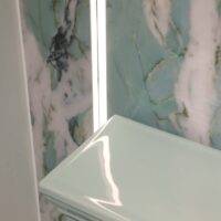 Detail of green porcelain feature wall with integrated LED lighting, green toilet top, black nickel toilet flush
