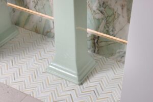 Marble floor tile in herringbone pattern in green powder room, porcelain feature wall with integrated LED lighting