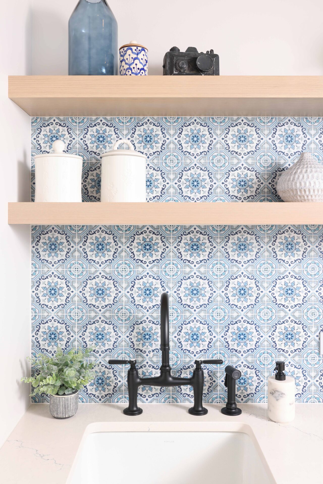 Matte black bridge faucet, blue pattern tile backsplash splash, rift cut white oak floating shelves