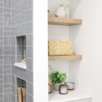 Storage niche with floating shelves and lower cabinet next to soft gray tile shower with two shower niches
