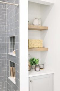 Storage niche with floating shelves and lower cabinet next to soft gray tile shower with two shower niches