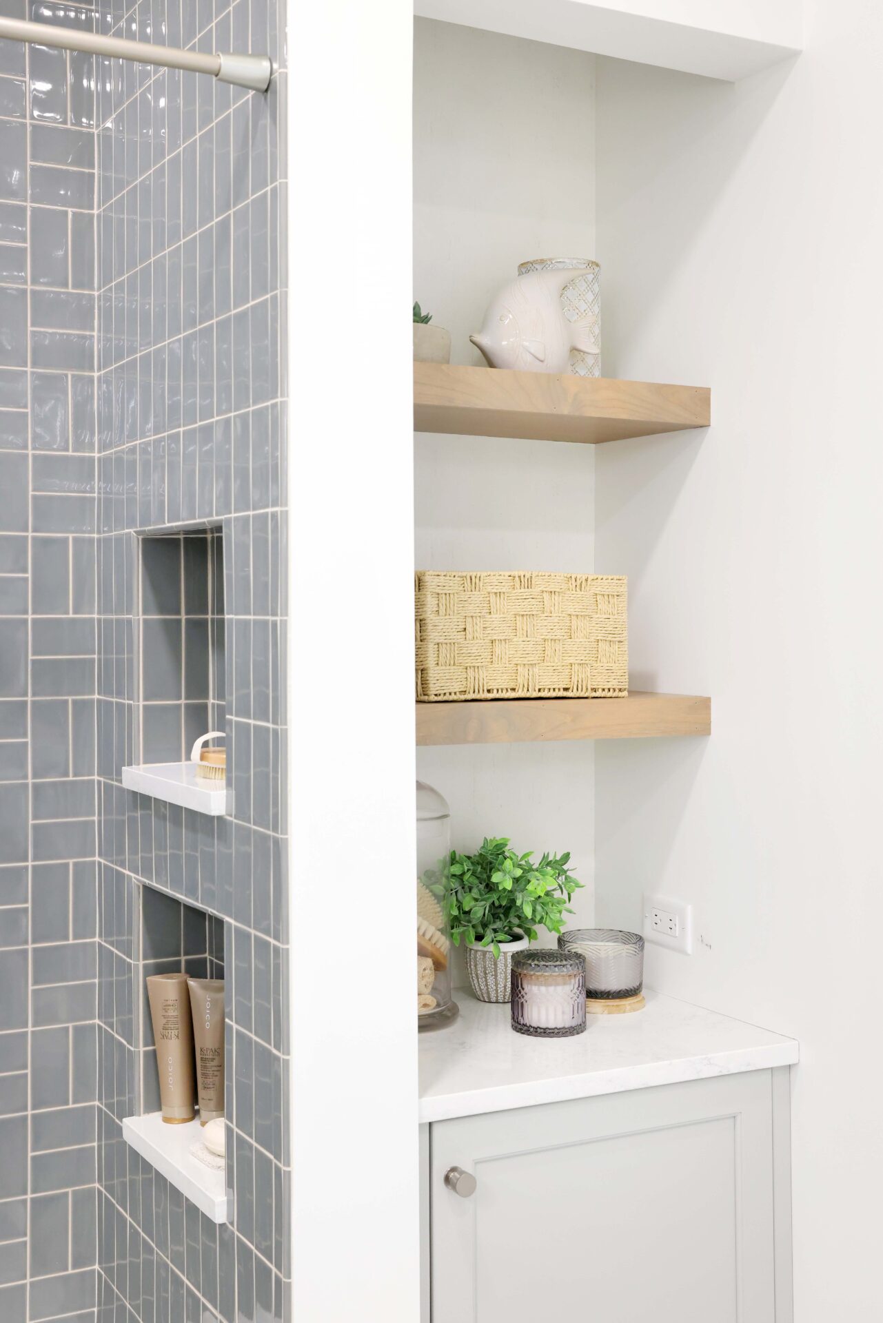 Storage niche with floating shelves and lower cabinet next to soft gray tile shower with two shower niches