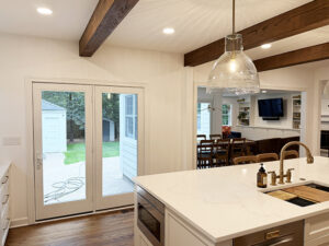 White kitchen with wood ceiling beams, POV into family room addition