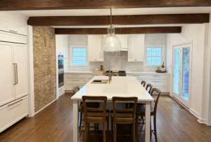 White kitchen with wood ceiling beams, exposed brick wall
