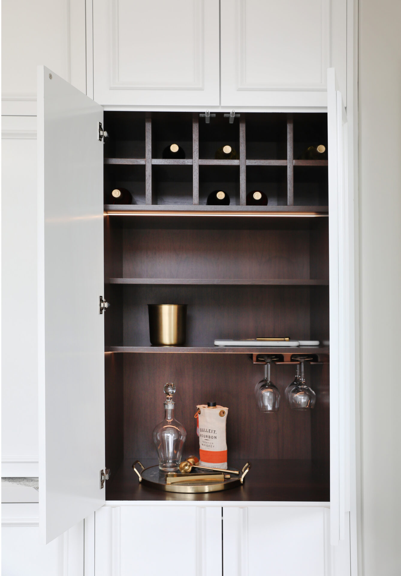 This liquor cabinet includes spaces for wine bottles and hanging storage for wine glasses.