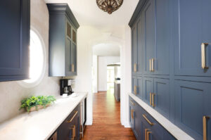 Updated traditional kitchen: The adjacent Butler’s pantry is accessed through an arched doorway. A wall of bold, navy-blue cabinets – including three garages for small appliances – addresses the need for more storage, while interior cabinet lighting ensures easy visibility on every shelf. Honey bronze cabinet hardware completes the look.