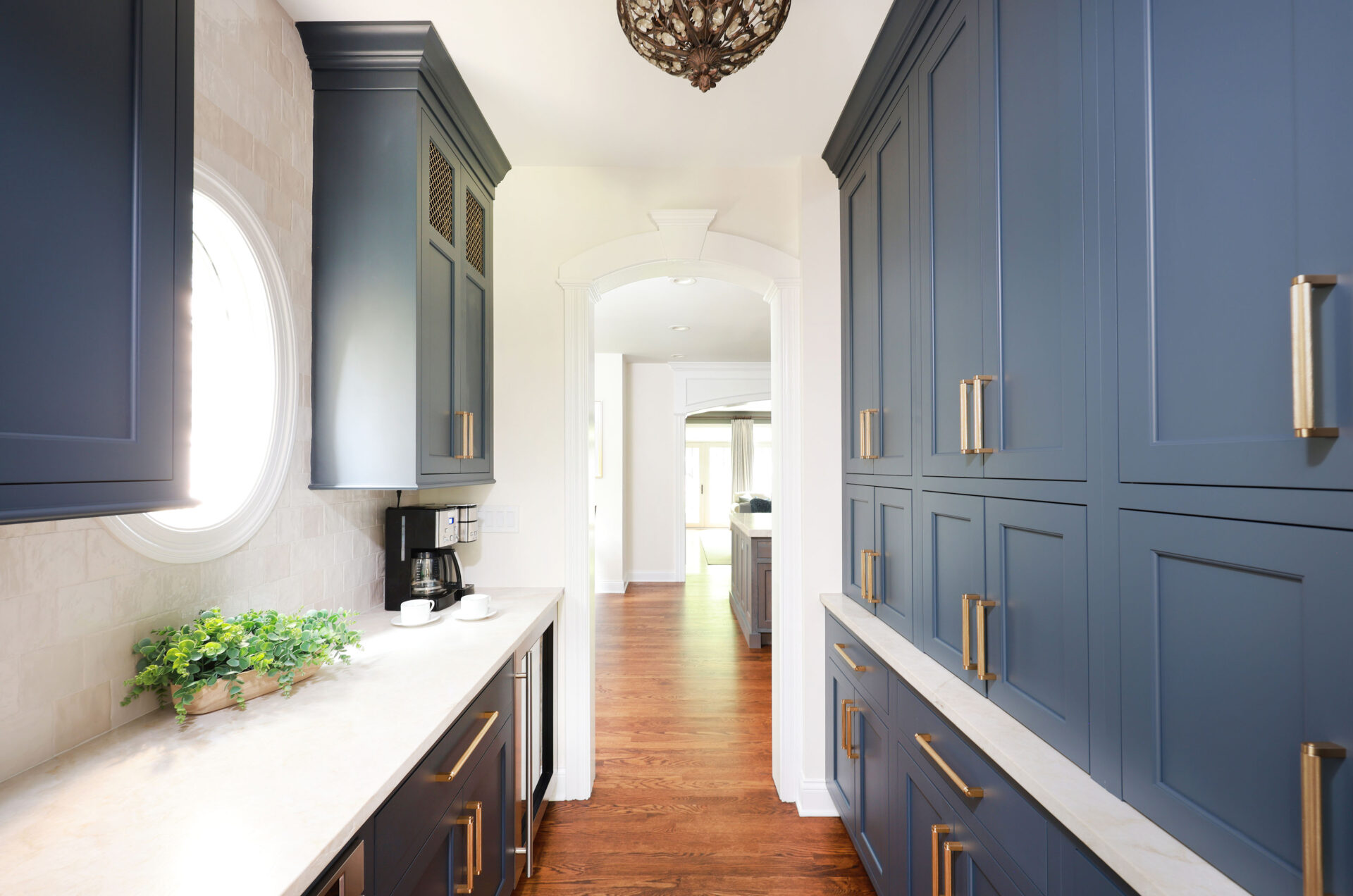 Updated traditional kitchen: The adjacent Butler’s pantry is accessed through an arched doorway. A wall of bold, navy-blue cabinets – including three garages for small appliances – addresses the need for more storage, while interior cabinet lighting ensures easy visibility on every shelf. Honey bronze cabinet hardware completes the look.