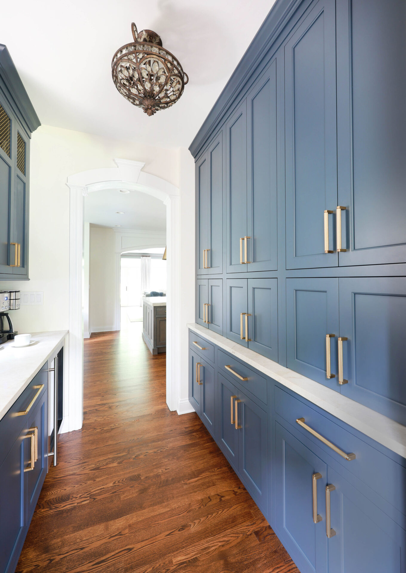 Updated traditional kitchen: In the Butler's pantry, bold, navy-blue cabinets contrast beautifully with off-white countertops, gold-bronze accents, and wood flooring.