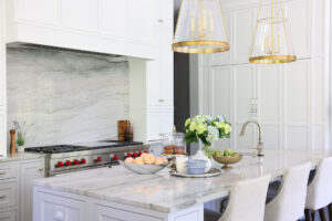 Paneled white refrigerator, polished nickel hardware and faucet on kitchen island sink, gold kitchen island lighting