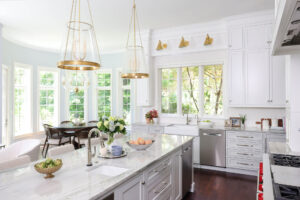 White kitchen with farmhouse sink, prep sink on island, quartzite countertops, gold fixtures