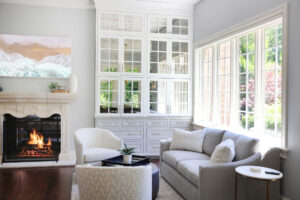 Fireplace with TV above, windows looking into backyard, kitchen couch, white and gray