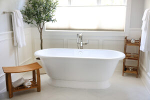 White freestanding tub with floor mounted faucet in polished nickel, volcanic limestone stone, wainscoting, tub below window