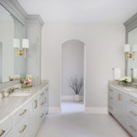 White and light gray primary bath with two vanities, gold sconces