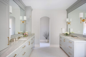 White and light gray primary bath with two vanities, gold sconces