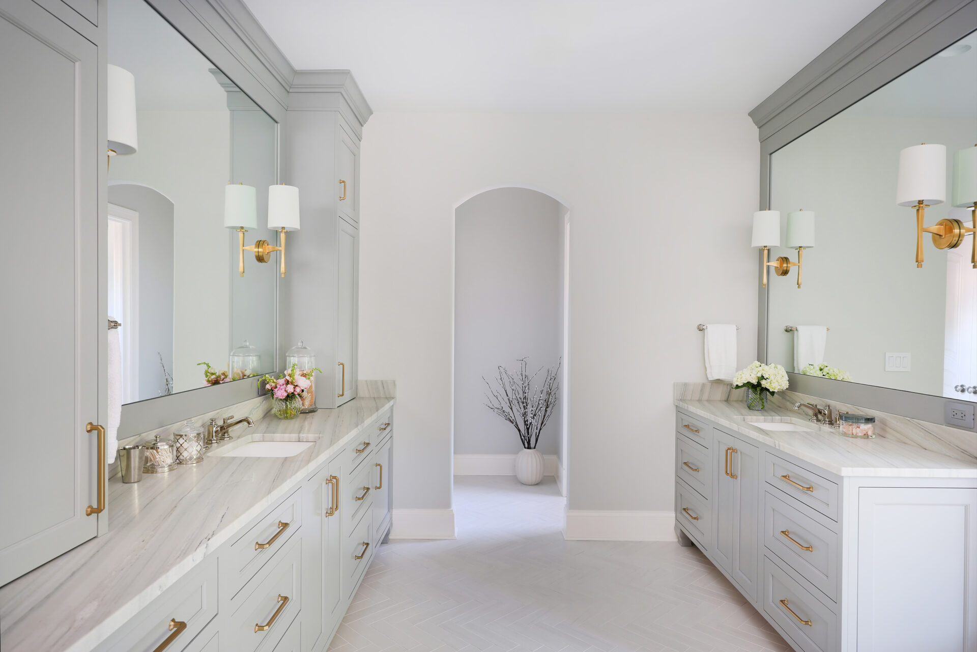White and light gray primary bath with two vanities, gold sconces