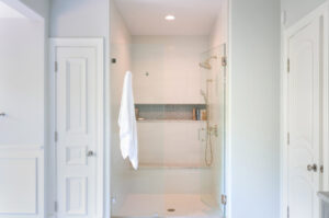 White shower with gray geometric tile shower niche and bench, polished nickel hardware