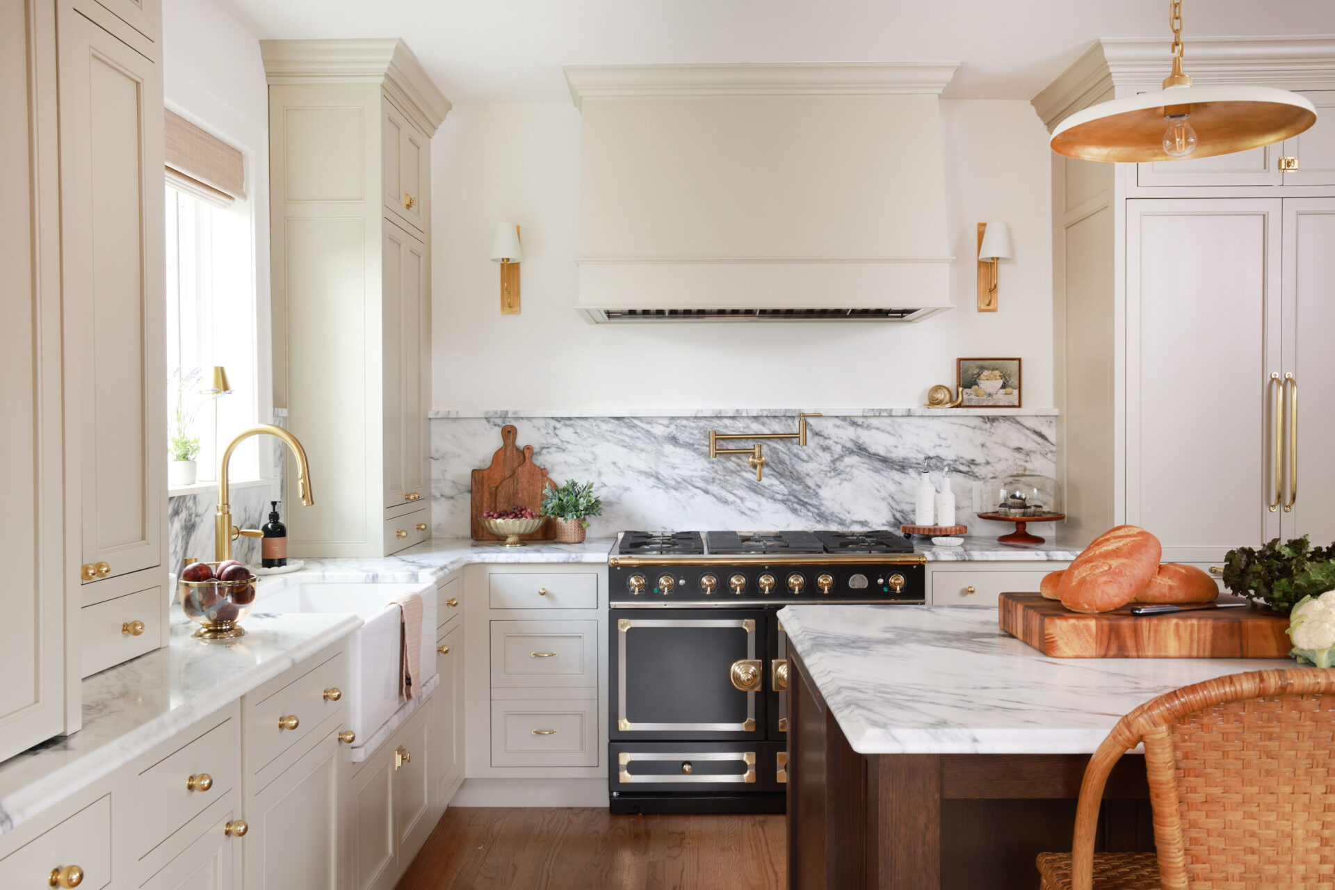 Warm white kitchen with modern vintage details, black and brass statement range, marble countertops and backsplash with shelf, pot filler, red oak island, island seating, farmhouse sink, paneled fridge, wood hood, with sconces, brass hardware and knobs