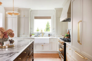 Warm white kitchen with modern vintage details, marble countertops, red oak island, farmhouse sink, with drip ledge, paneled fridge, brass hardware and knobs, to the ceiling cabinets, inset cabinetry, window above sink, set on backsplash in marble