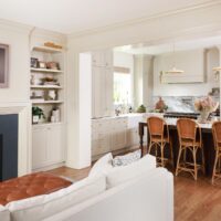 Open concept kitchen and family room, warm white cabinetry, kitchen island with seating, built in shelves on side of fireplace with picture light fixture, blue fireplace face