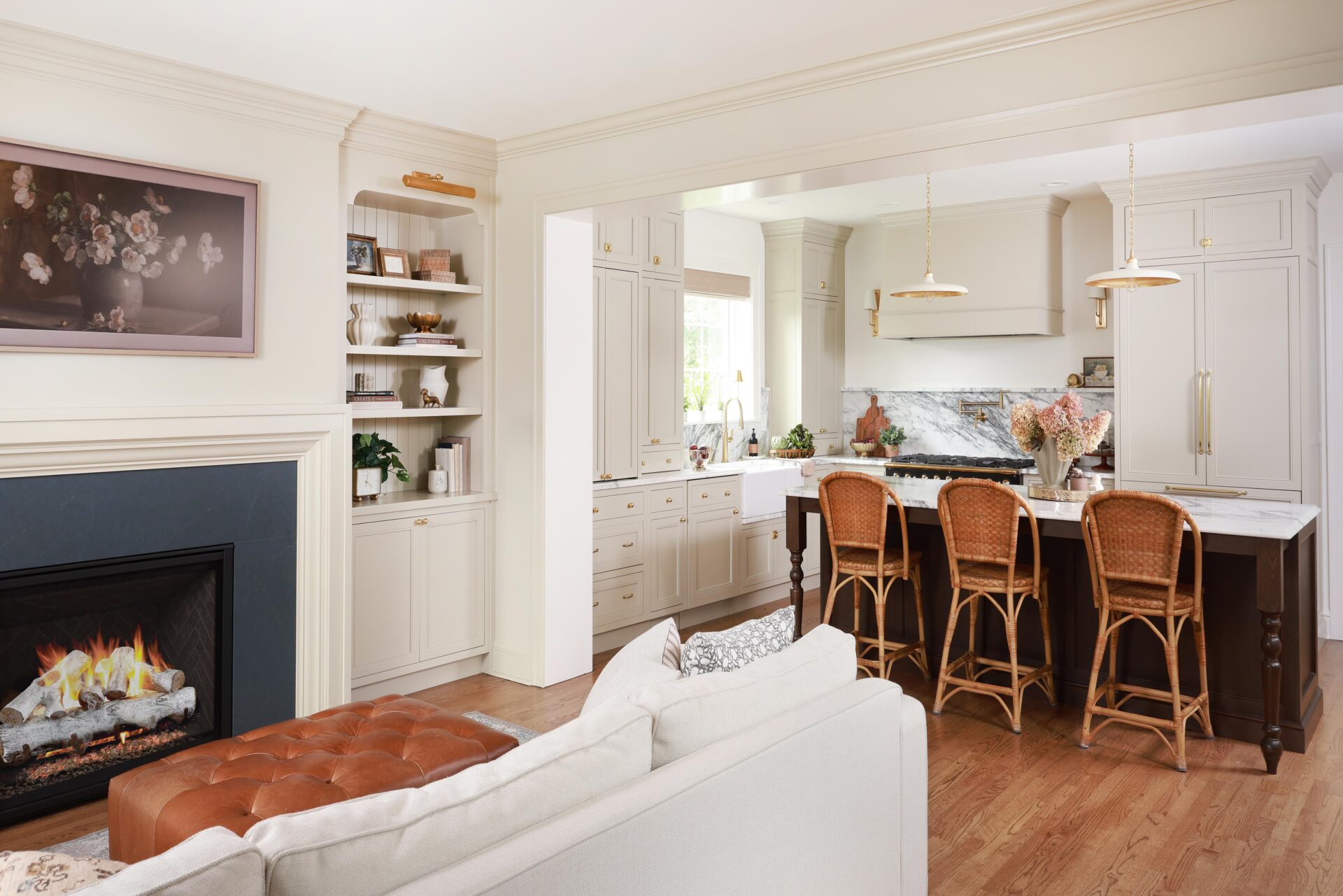Open concept kitchen and family room, warm white cabinetry, kitchen island with seating, built in shelves on side of fireplace with picture light fixture, blue fireplace face