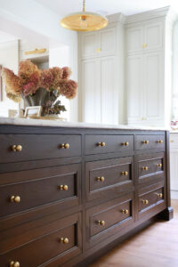 Red oak kitchen island with dark stain, drawers with brass knobs, warm white to-the-ceiling cabinets in warm white