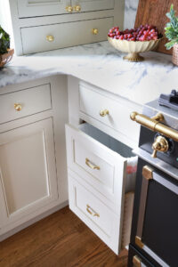 Hidden paneled trash can, warm white cabinetry, brass hardware and knobs, marble countertops