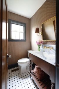 Powder room with marble countertop, oak vanity, brass wall-mounted faucet, wallpaper, balck and white tile floor